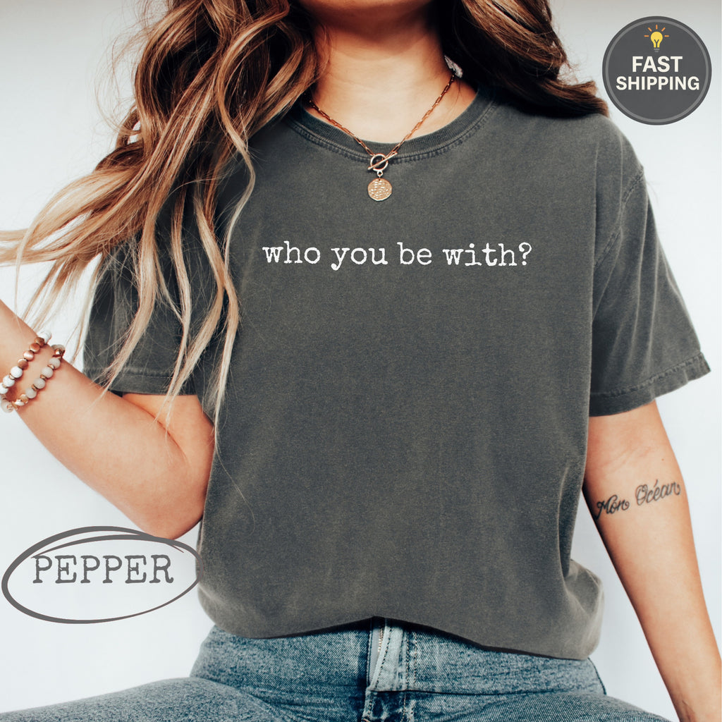 Woman wearing dark grey t-shirt with "who you be with?" text.