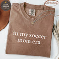 Brown t-shirt with "in my soccer mom era" text.
