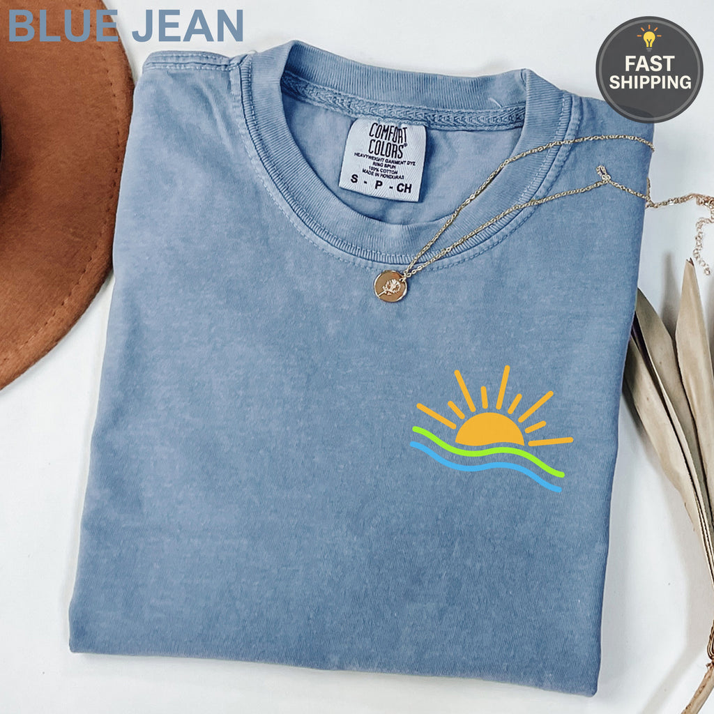 Blue Jean Comfort Colors t-shirt with sun and waves graphic on chest.