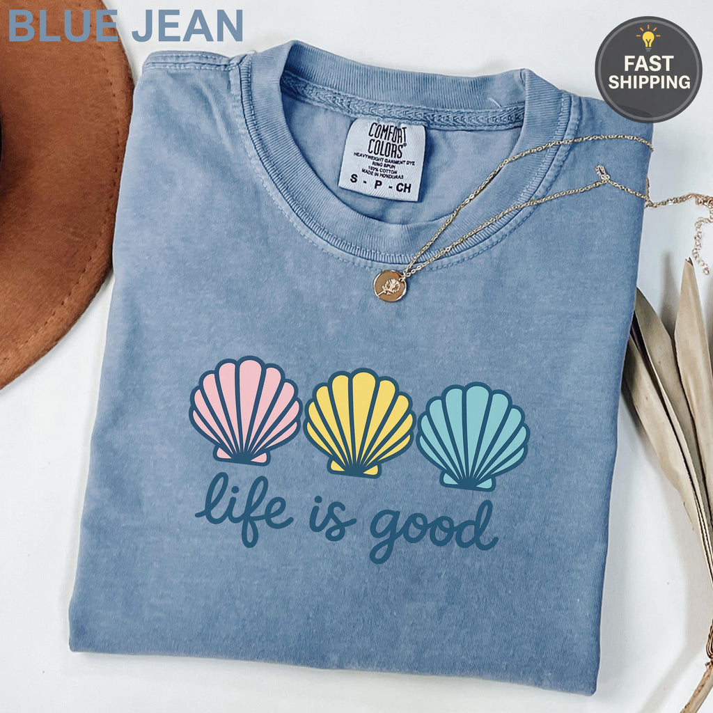 Blue Jean Comfort Colors t-shirt with "life is good" and three seashells.